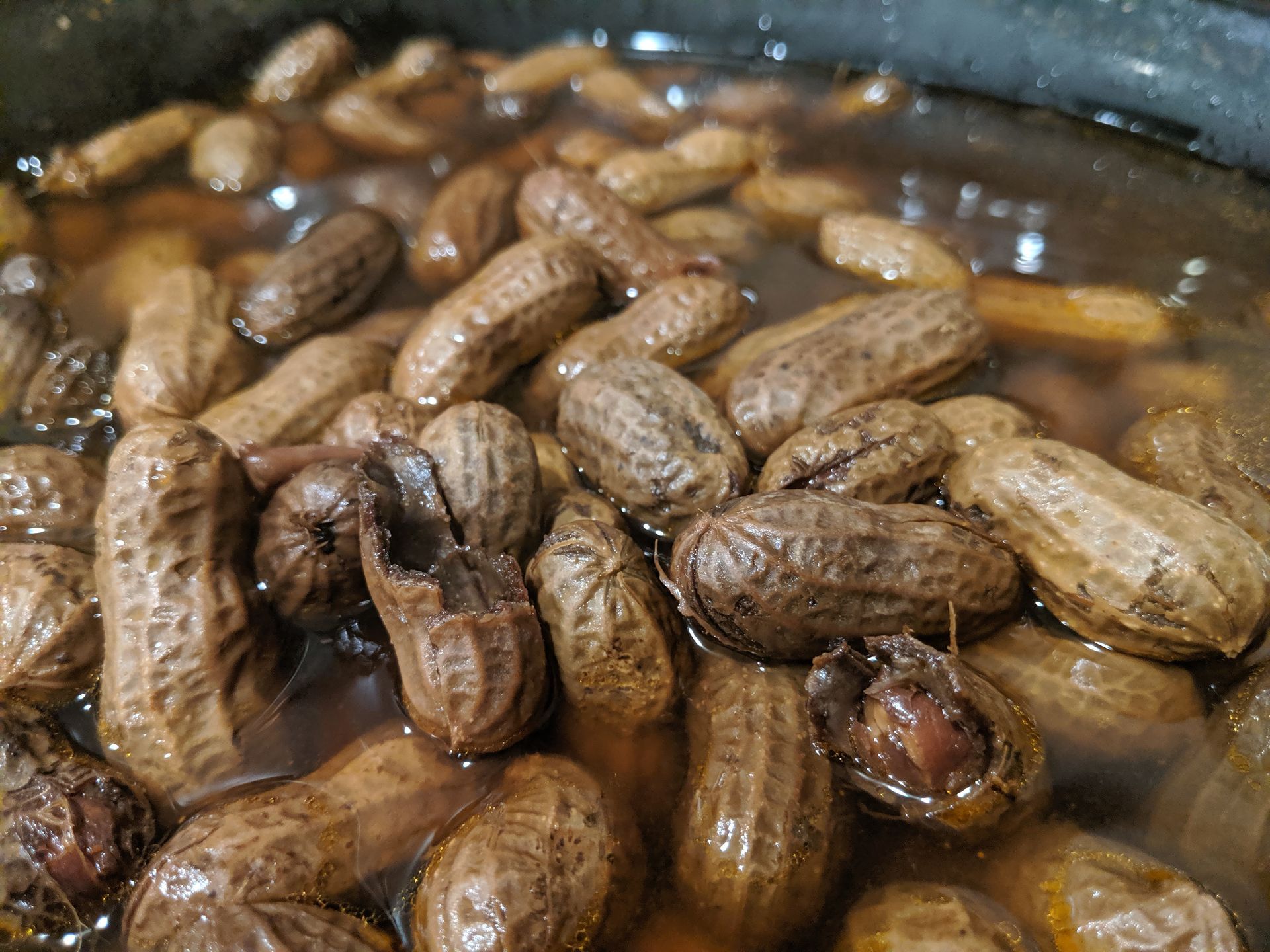 Boiled peanuts in a dark broth, close-up, shells are textured and brown.