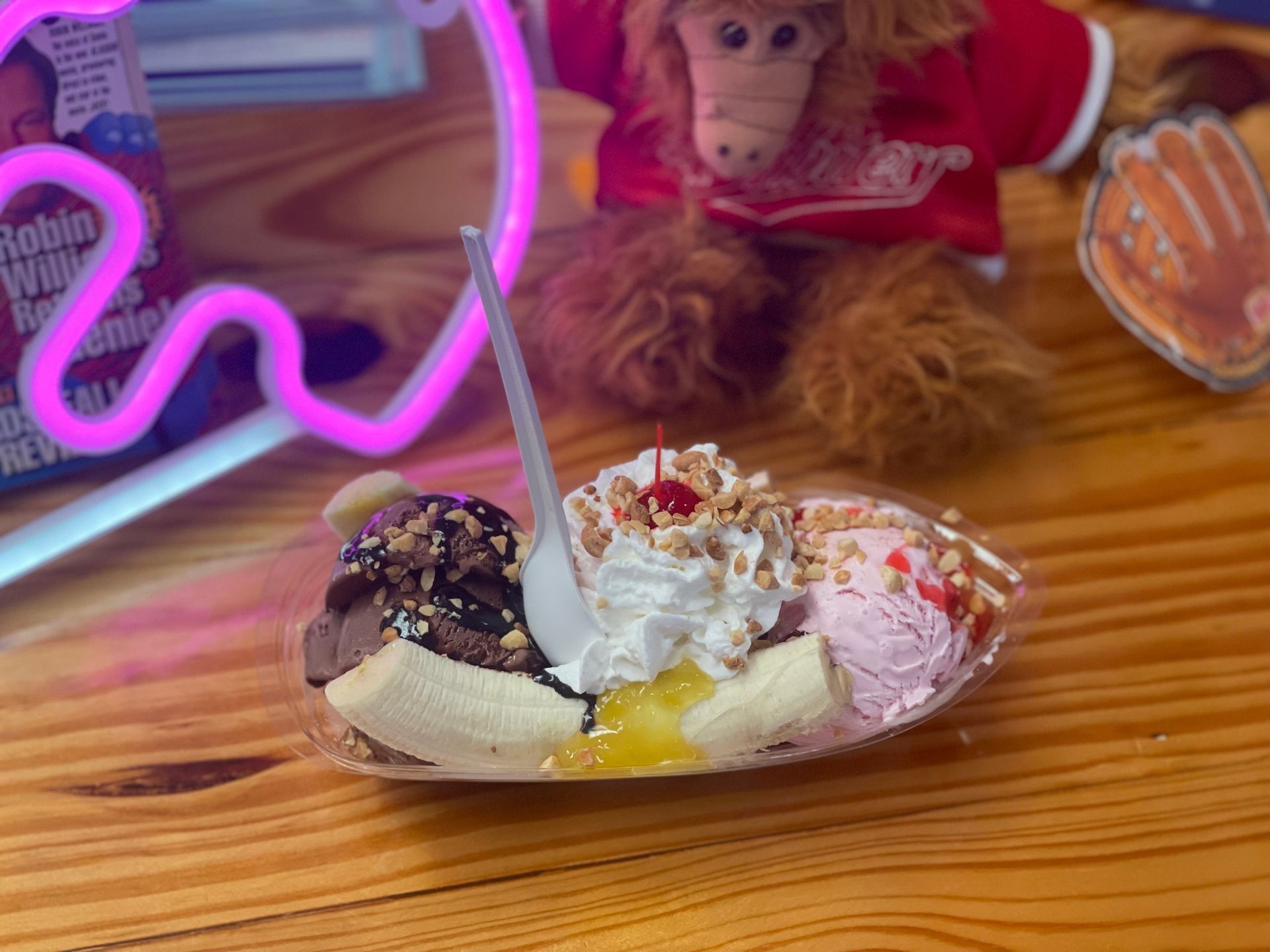 A banana split is on a wooden table next to a stuffed animal.