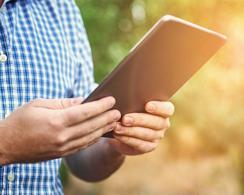 Person holding a tablet outdoors in warm sunlight