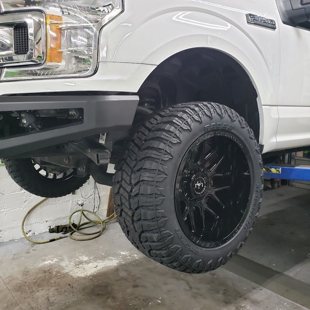 A white truck with black wheels and tires on a lift in a garage.