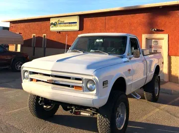 White lifted Chevrolet pickup truck parked outside a building with a sign.