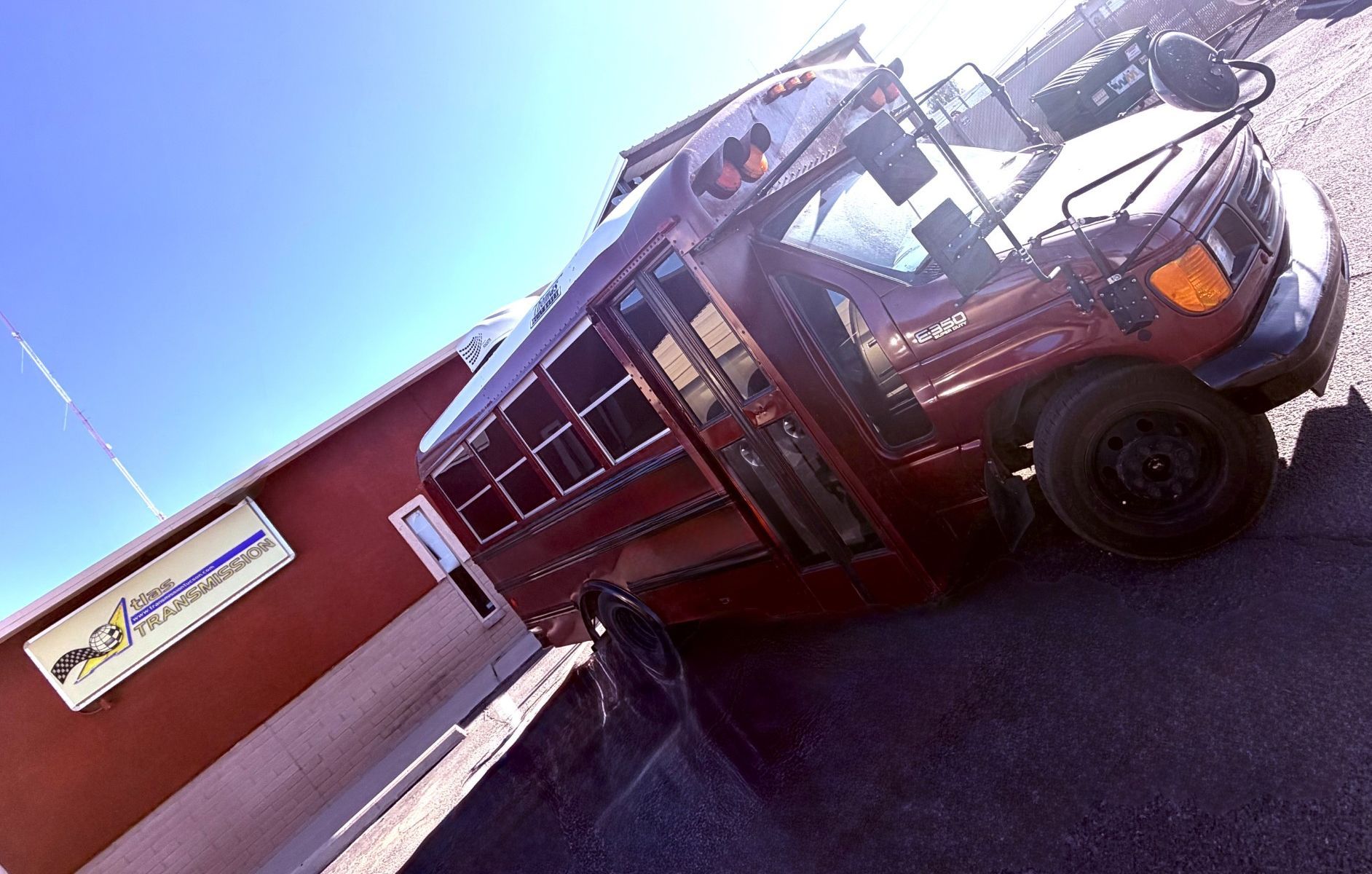 Red bus parked outside a building with a sign, shot at a tilted angle under bright sun