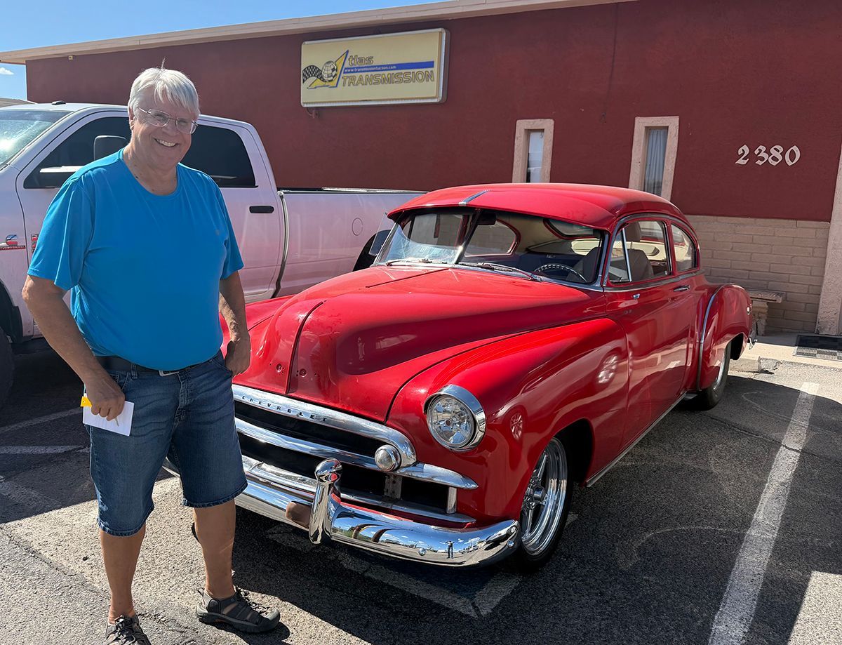 Man in blue shirt standing beside a red classic car in a parking lot