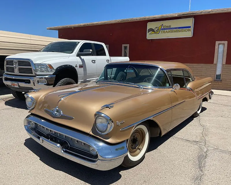 Gold vintage car parked in front of a building with a white pickup truck.