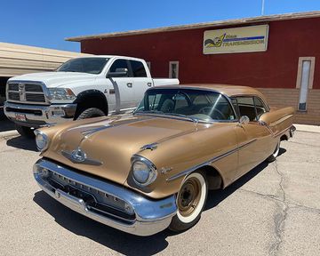 A gold car is parked in front of a red building next to a white truck.