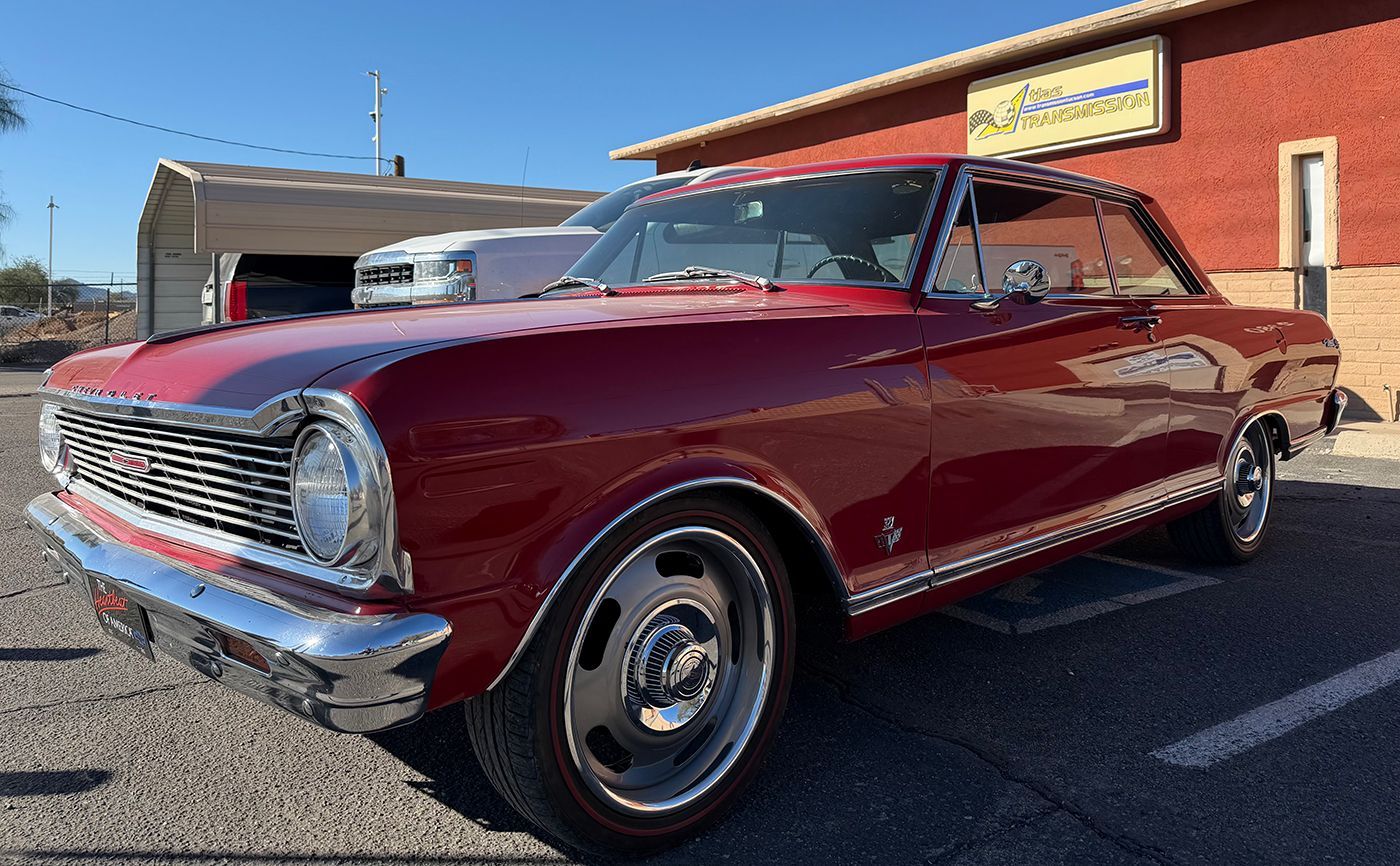 Burgundy Chevrolet Nova parked in front of a building with blue sky.