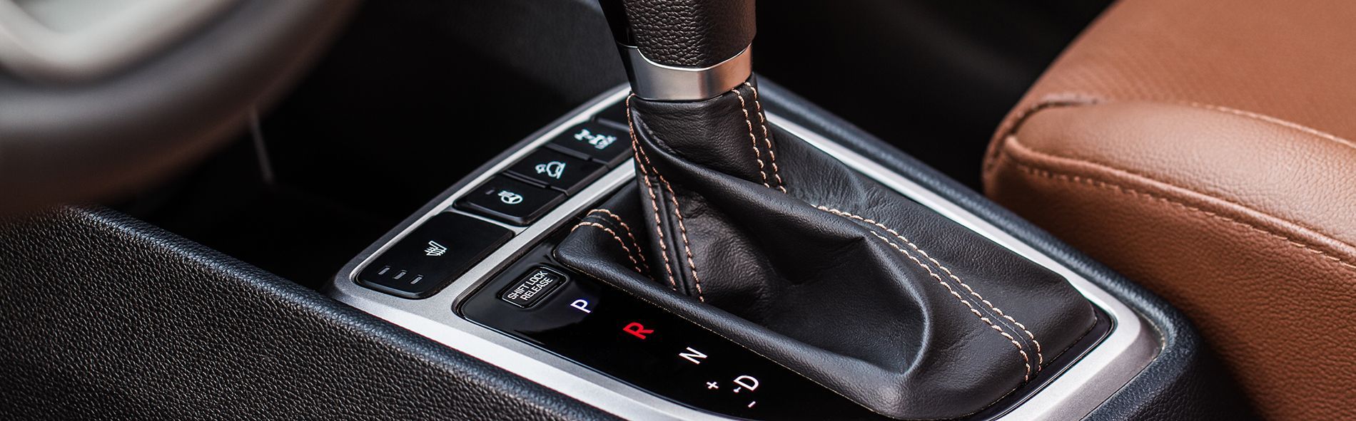 Close-up of a car's gear shift lever surrounded by buttons and a leather seat.
