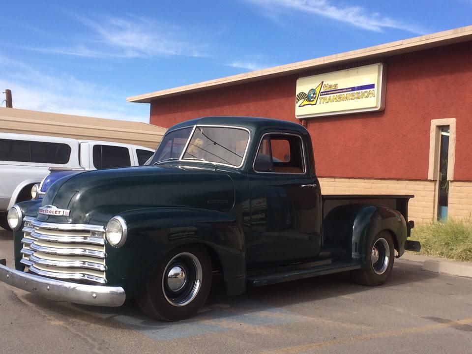 A green truck is parked in front of a red building.