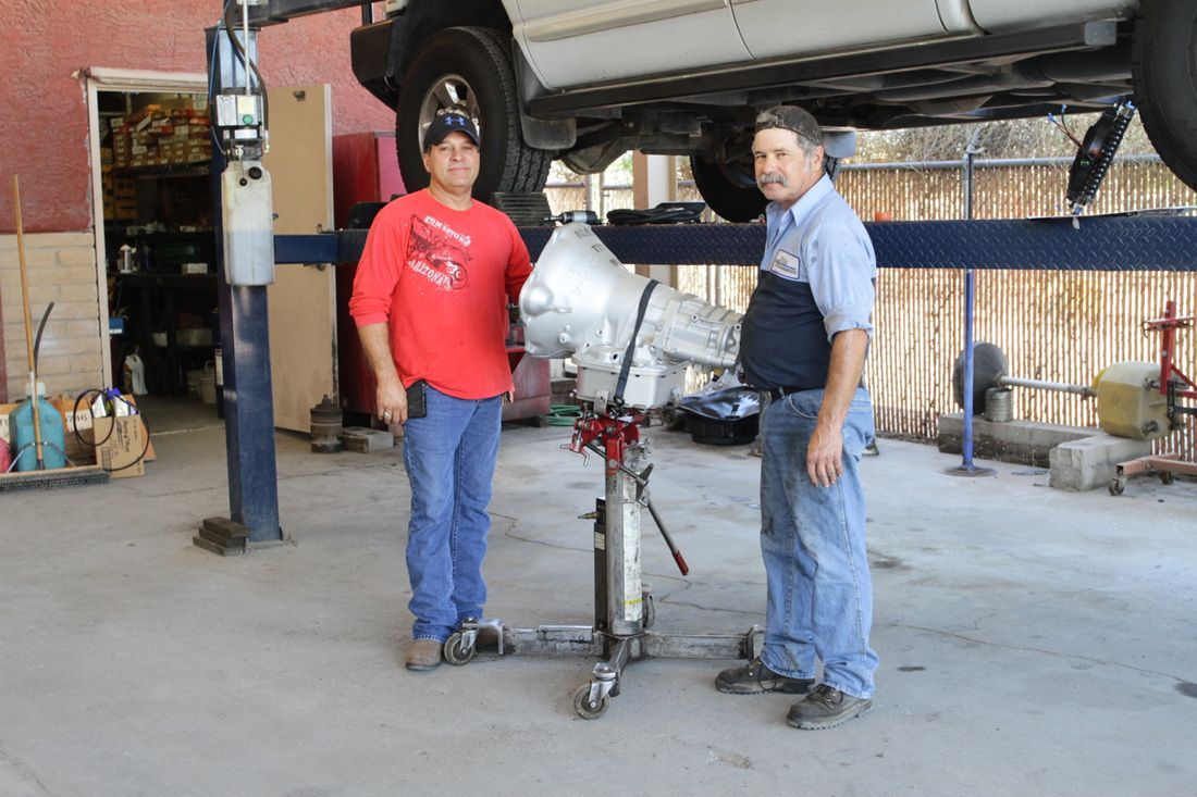 Two men are standing in front of a car on a lift in a garage.