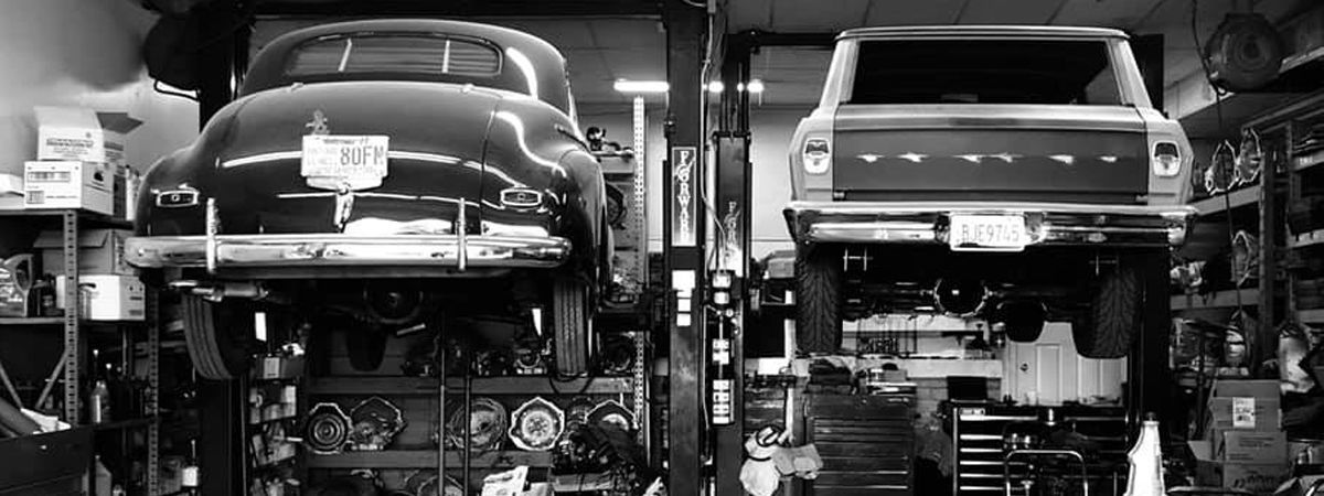 Two cars are sitting on a lift in a garage.