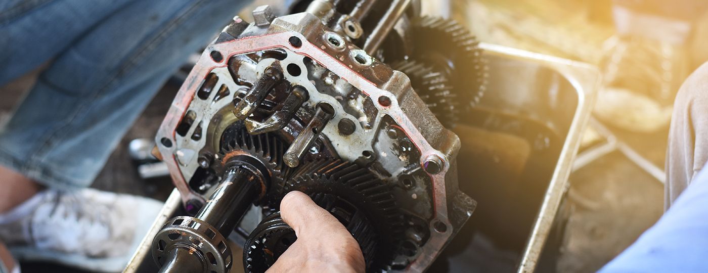 Mechanic holding a disassembled car transmission covered in oil.