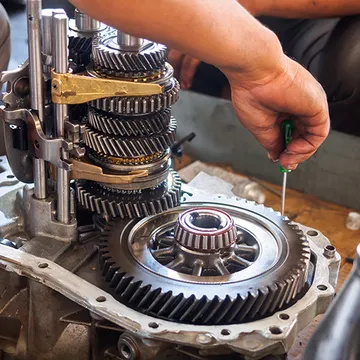 A man is working on a gearbox with a screwdriver.