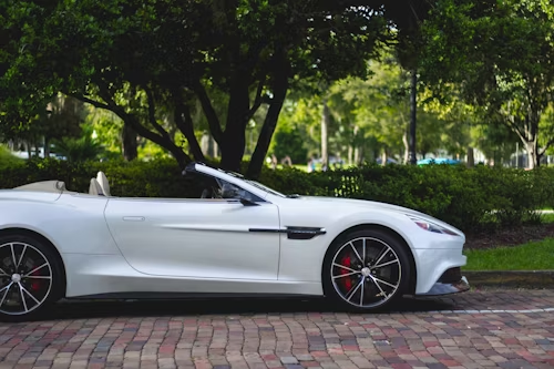 White convertible sports car parked on brick, with trees and greenery in the background.