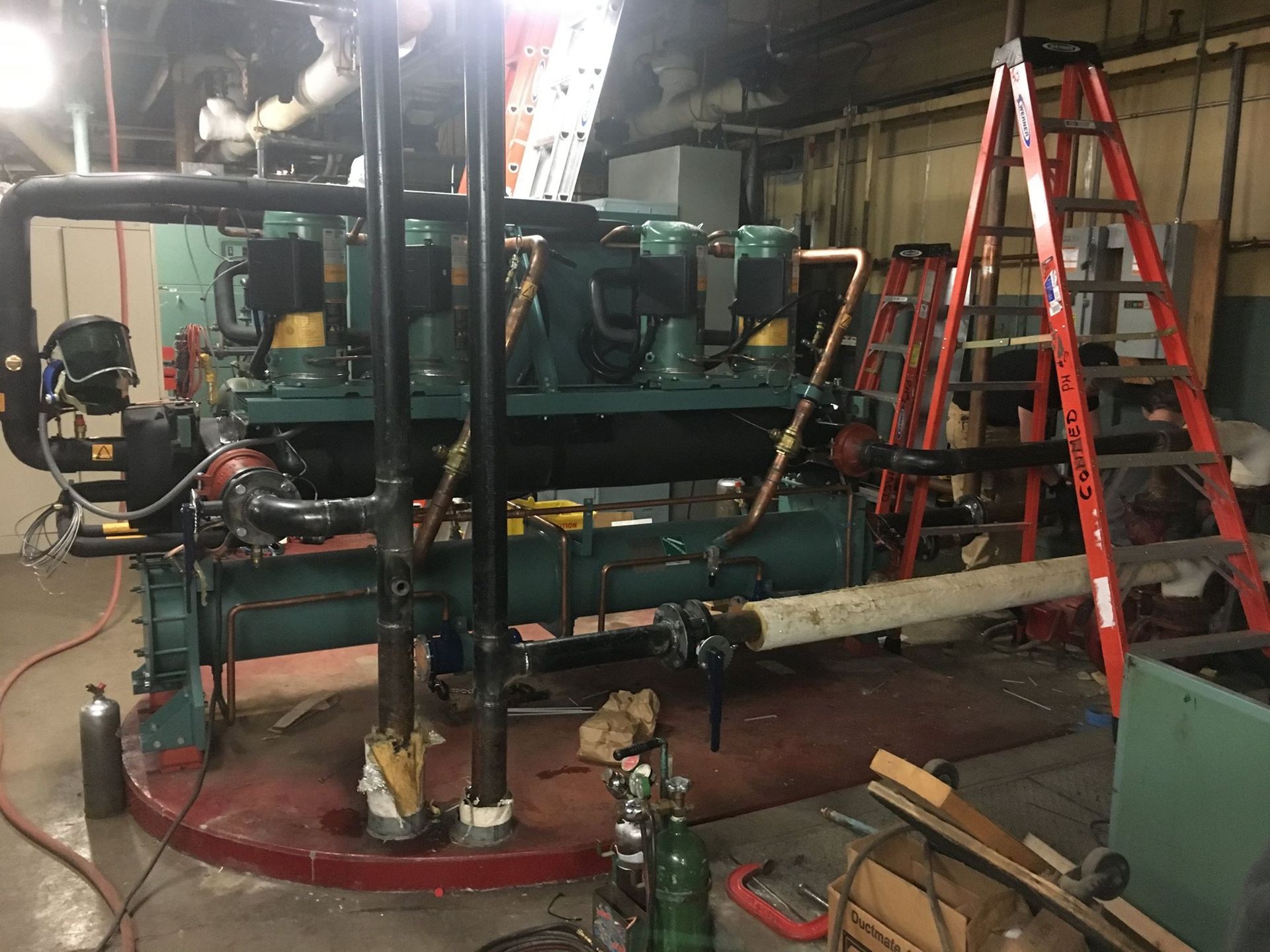 Large industrial chiller with pipes and a ladder in an indoor setting.