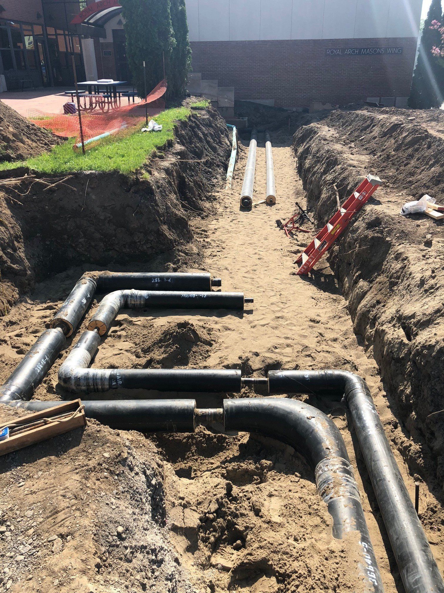 Pipes in a trench. Black pipes are being installed, white pipes run further back. Construction site.