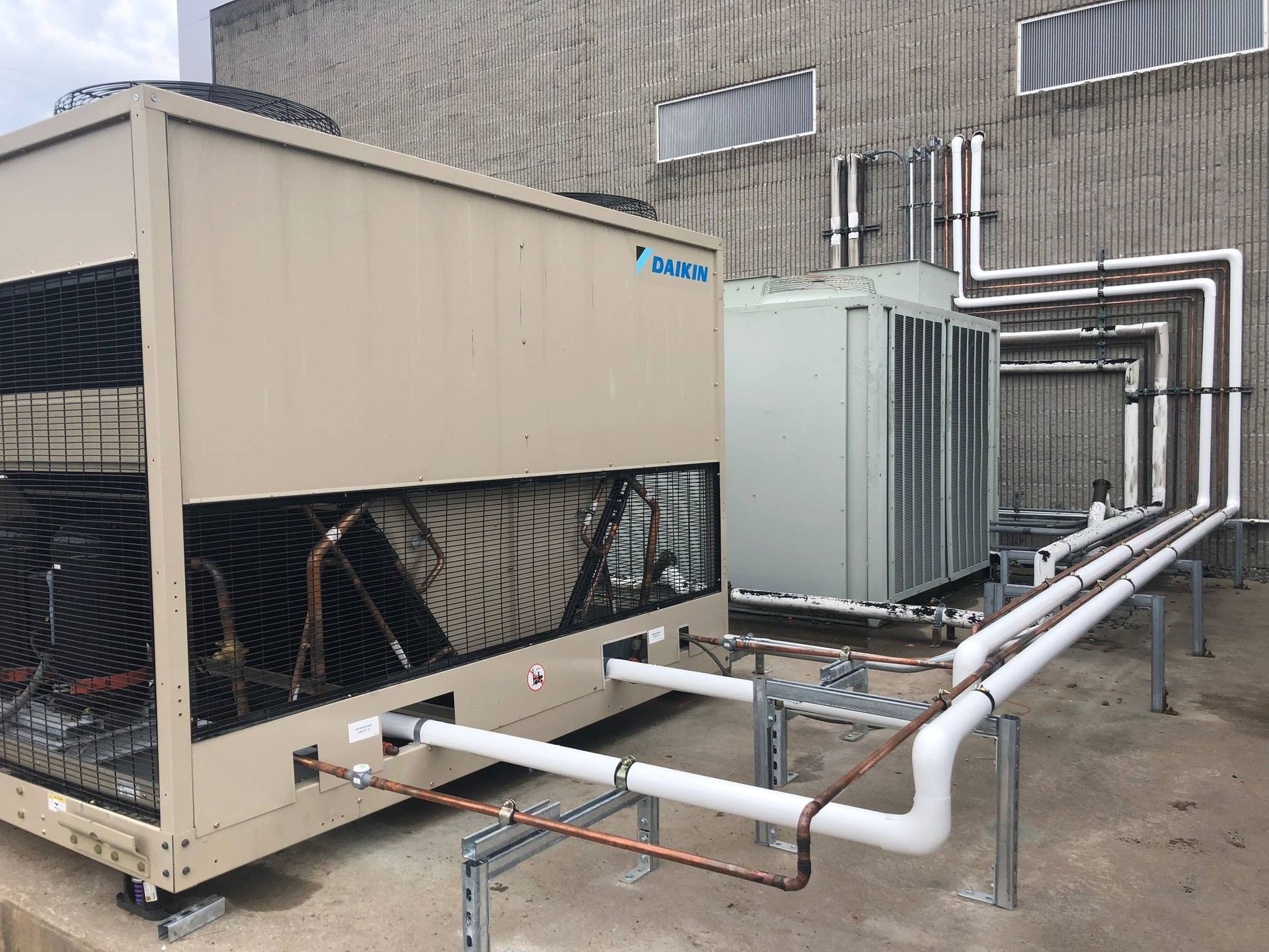 HVAC units on a building rooftop with connected white and copper pipes.