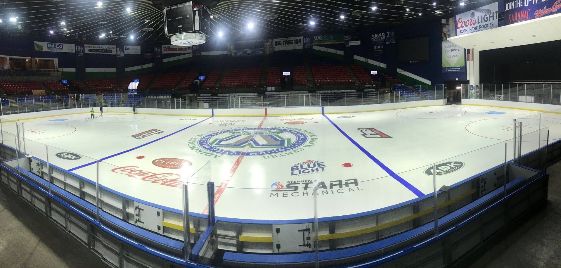 An ice hockey rink with players skating. Empty red seating surrounds the arena.