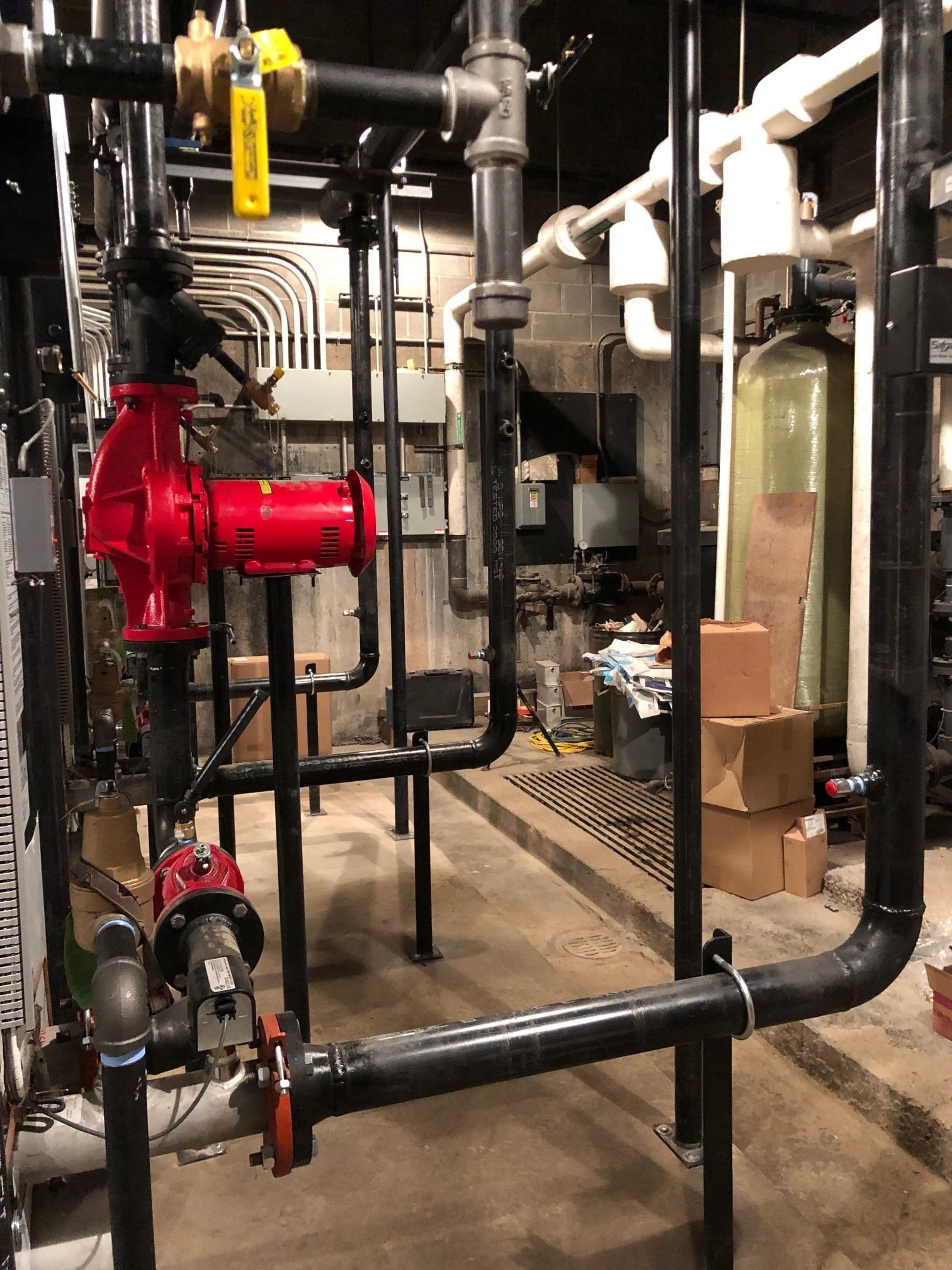 Red pump and black pipes in a mechanical room, with electrical conduits and a water filter.