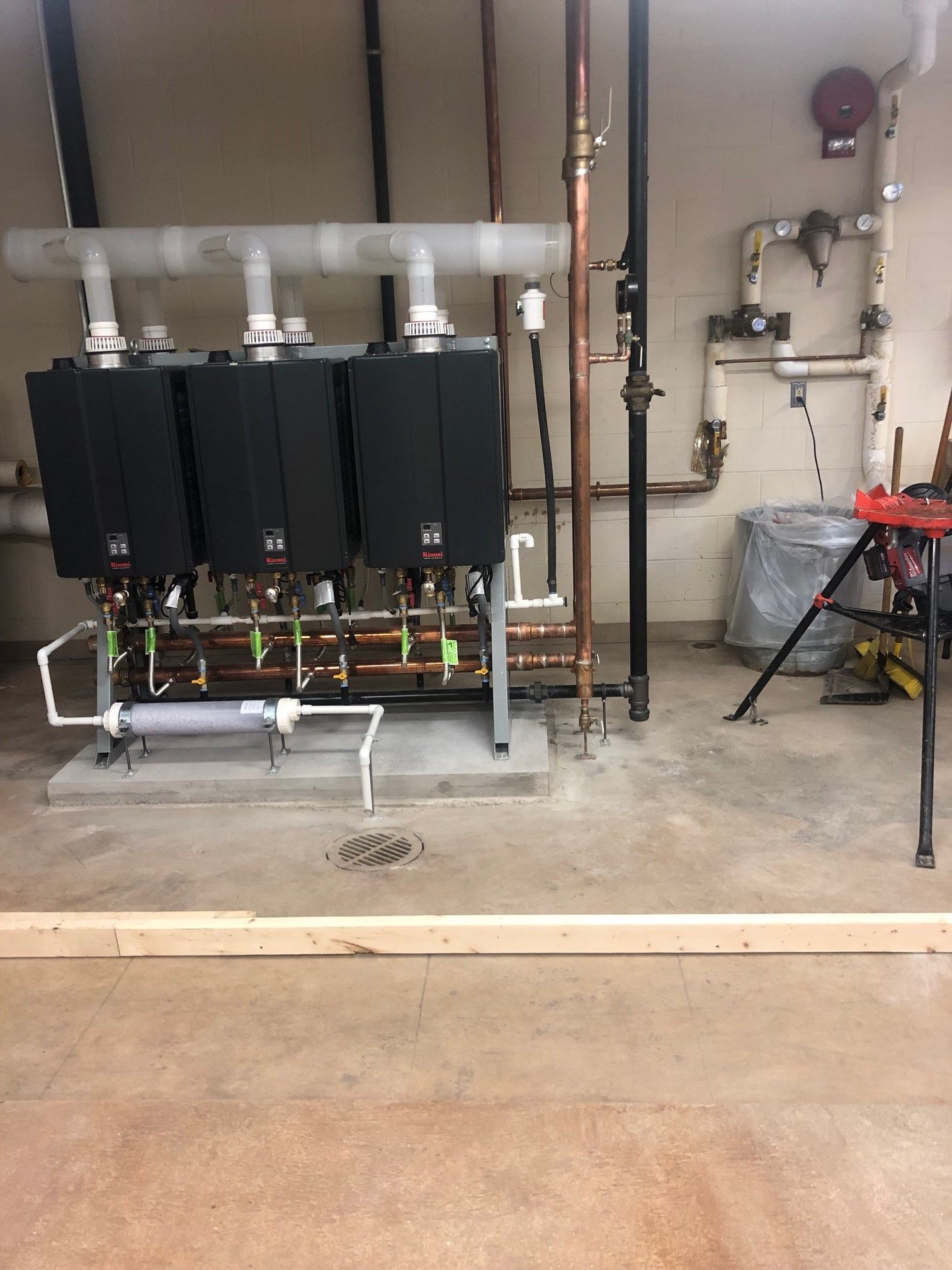 Three black water heaters with white pipes in a utility room. Copper and black piping. Concrete floor.