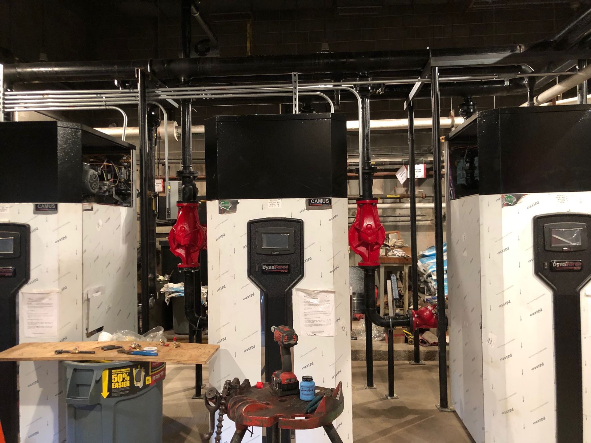 Three industrial water heaters in a mechanical room, with red valves and black piping.