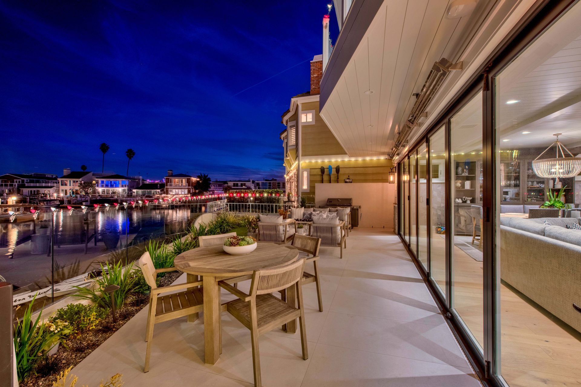 A scenic balcony at dusk with a round patio table overlooking a waterfront residential neighborhood with glowing lights.