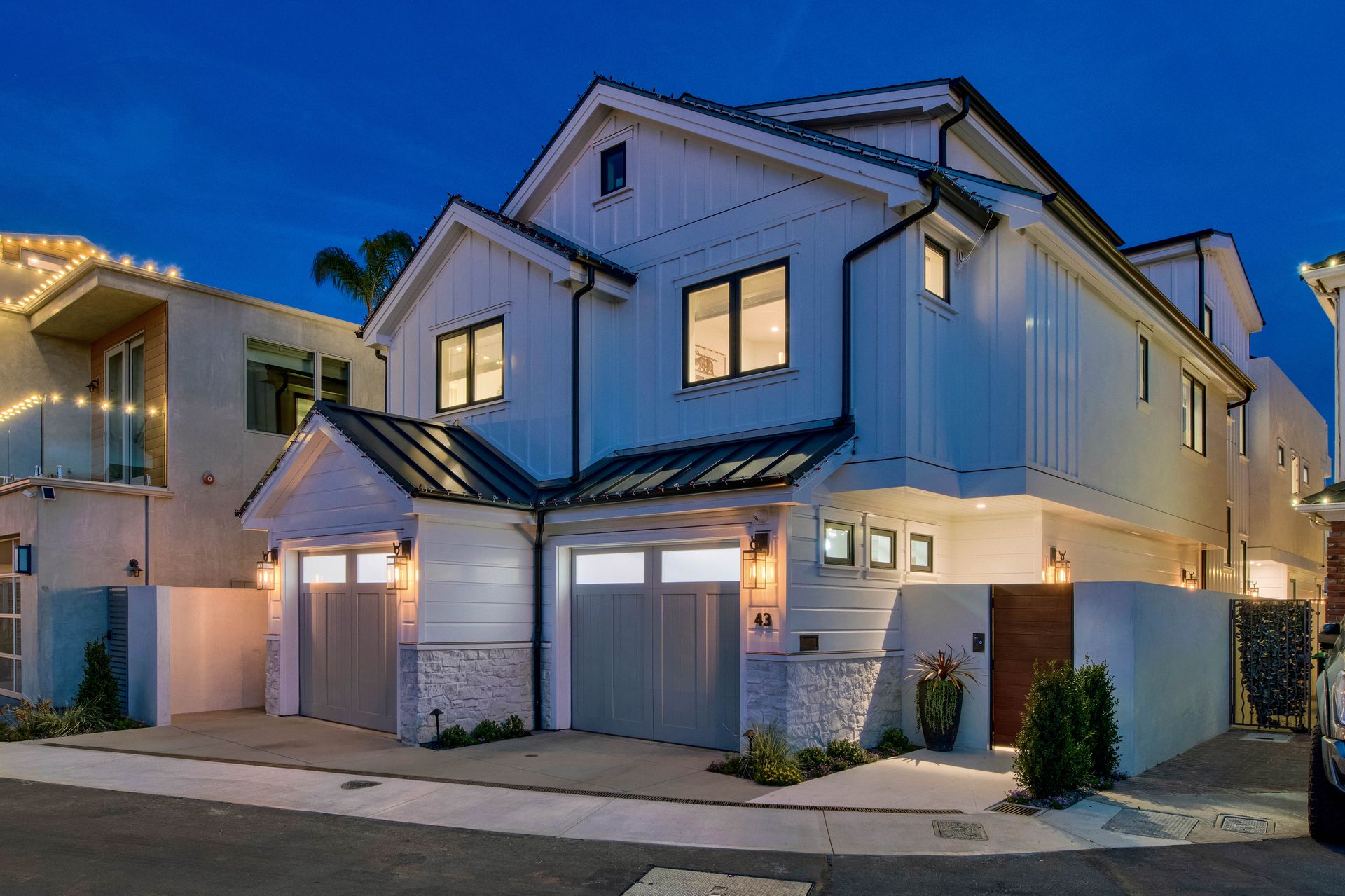 A modern two-story white house with black window frames and garage doors, illuminated at twilight.