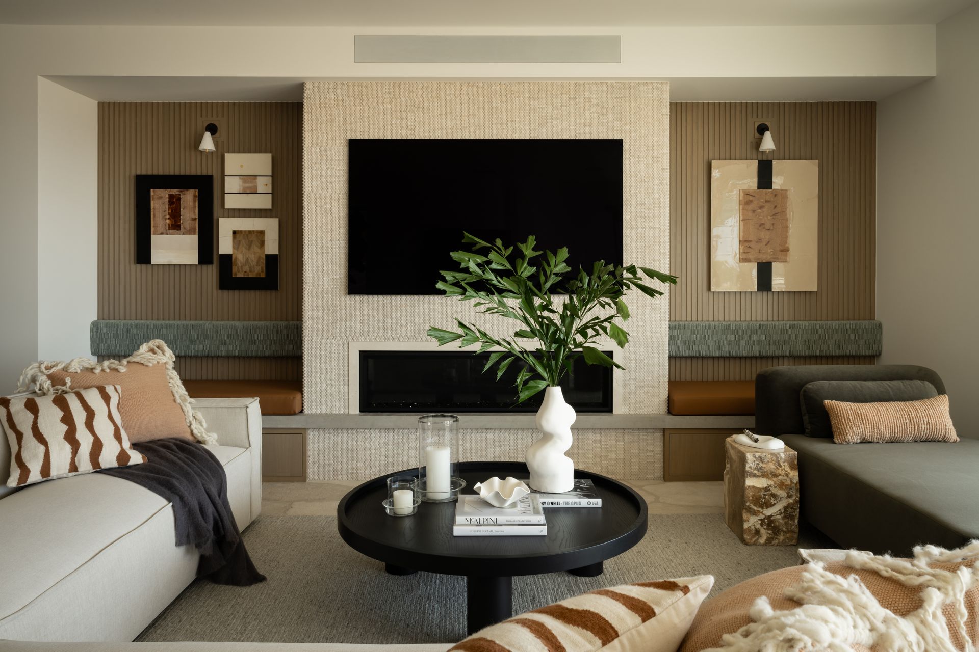 A modern living room with a TV above a fireplace, a round black coffee table, a white sofa, and a grey chaise longue.