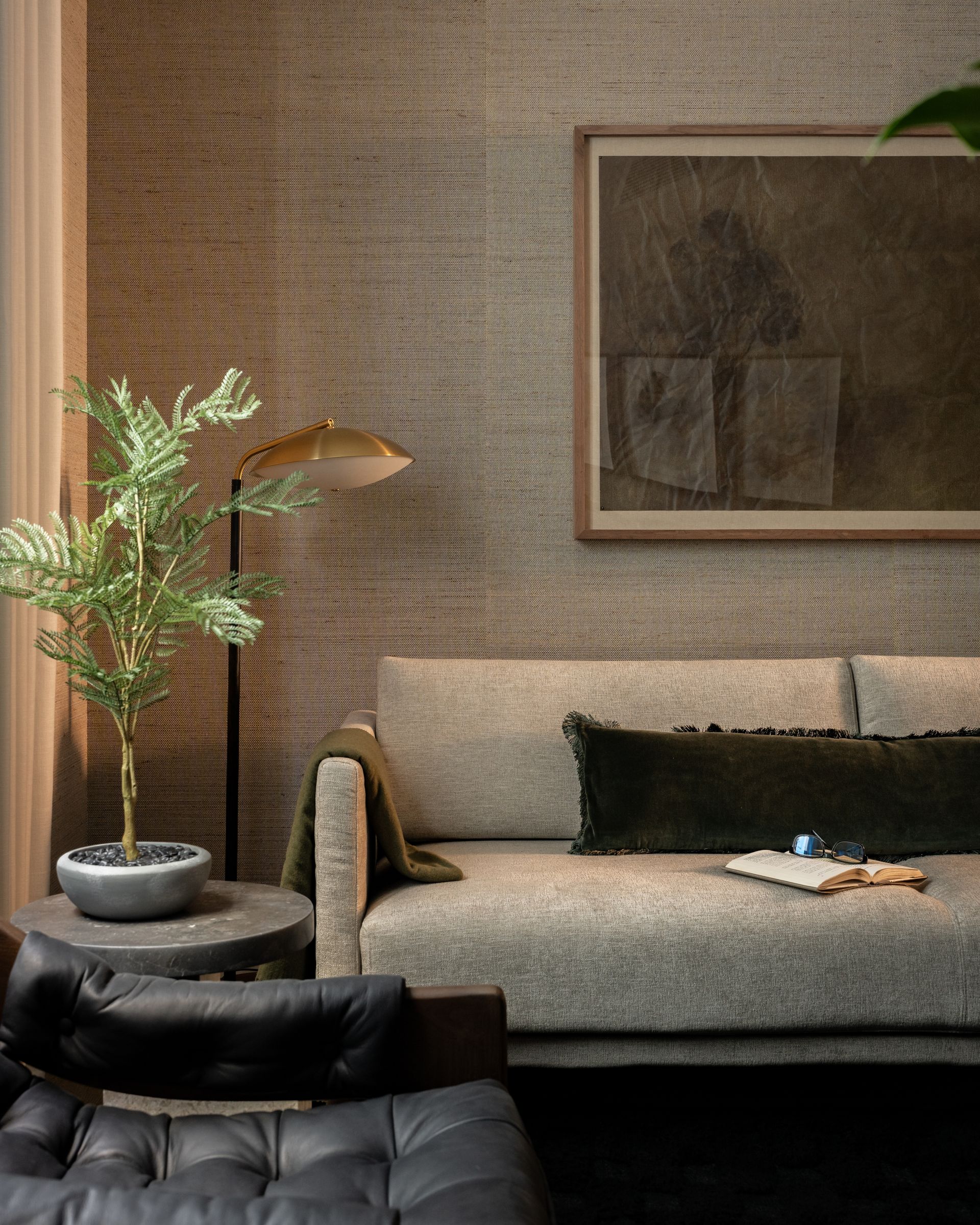 A neutral-toned living room features a textured wall, a light-colored sofa, a leather armchair, and a small potted plant.