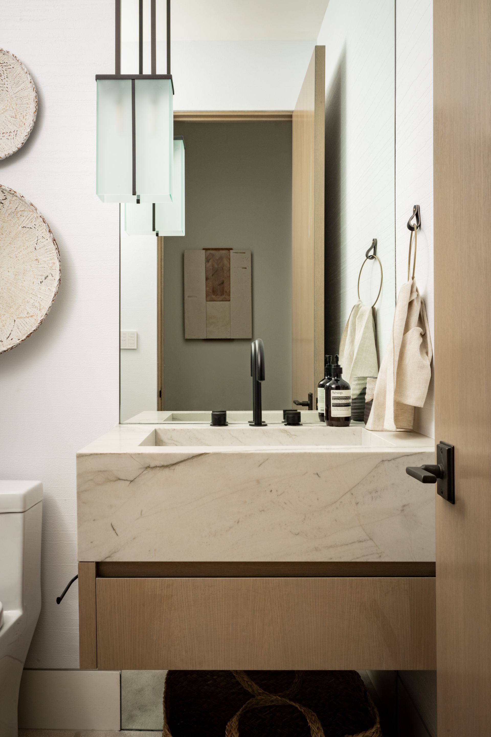 Modern bathroom with a stone basin, wood vanity, matte black faucet, and pendant lighting against a white wall.