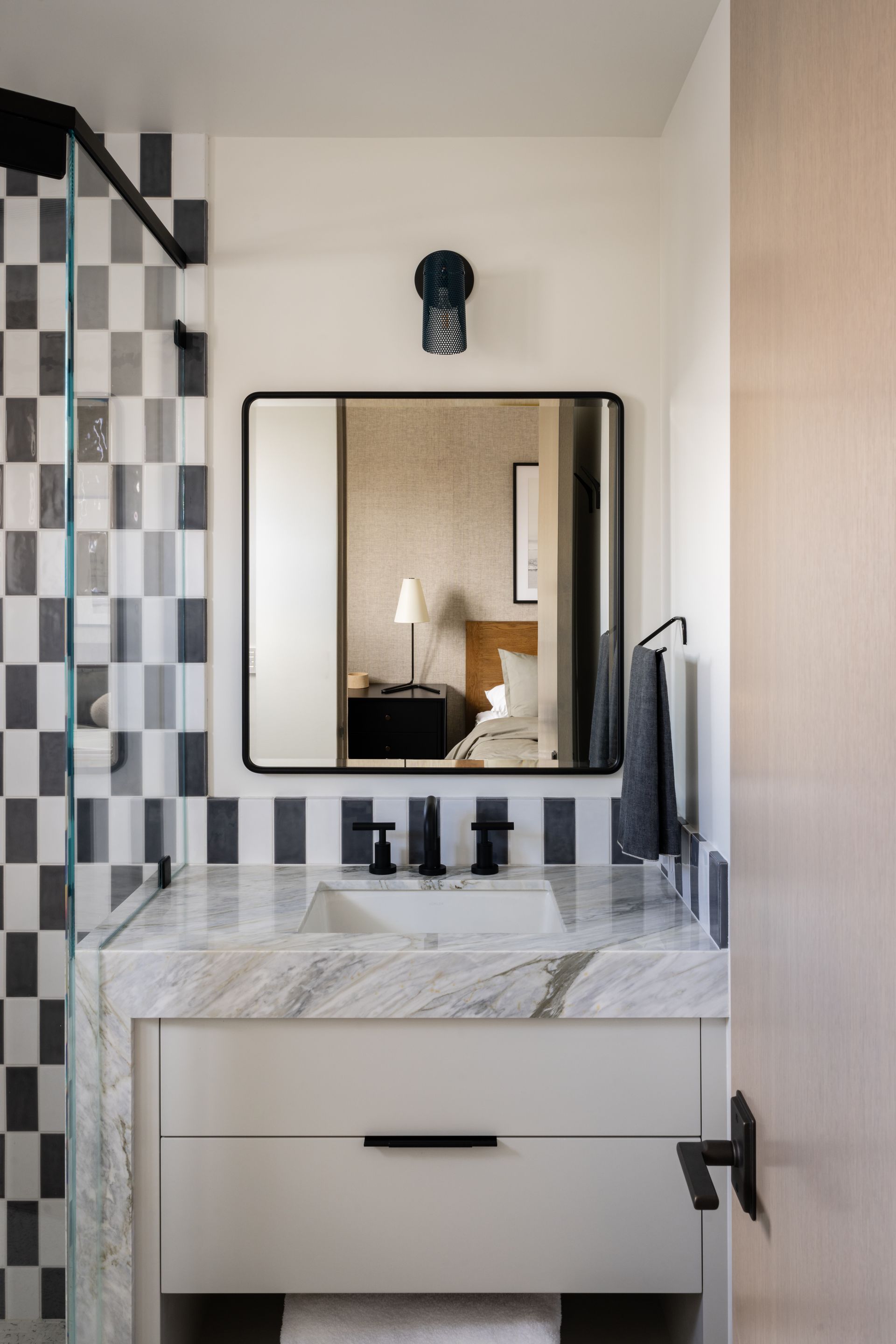 A modern bathroom vanity with a white marble countertop, black hardware, a square mirror, and black-and-white tiled walls.