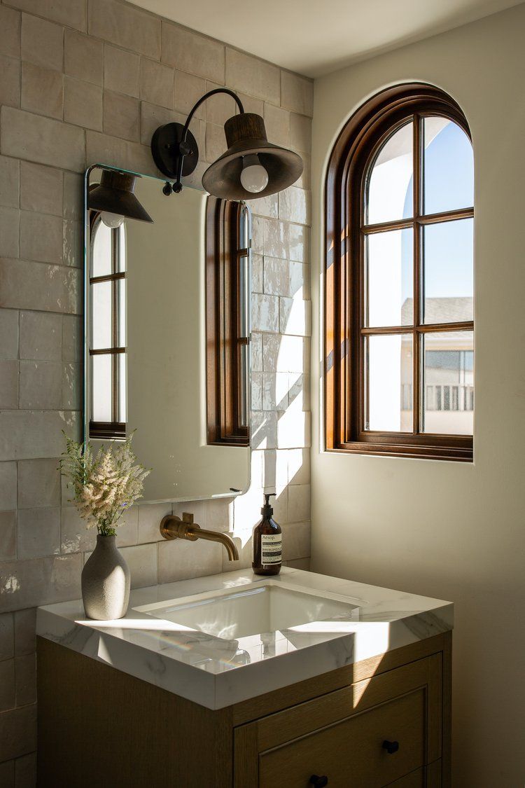 A modern bathroom vanity with a square sink, marble countertop, wall-mounted faucet, and arched window in natural light.