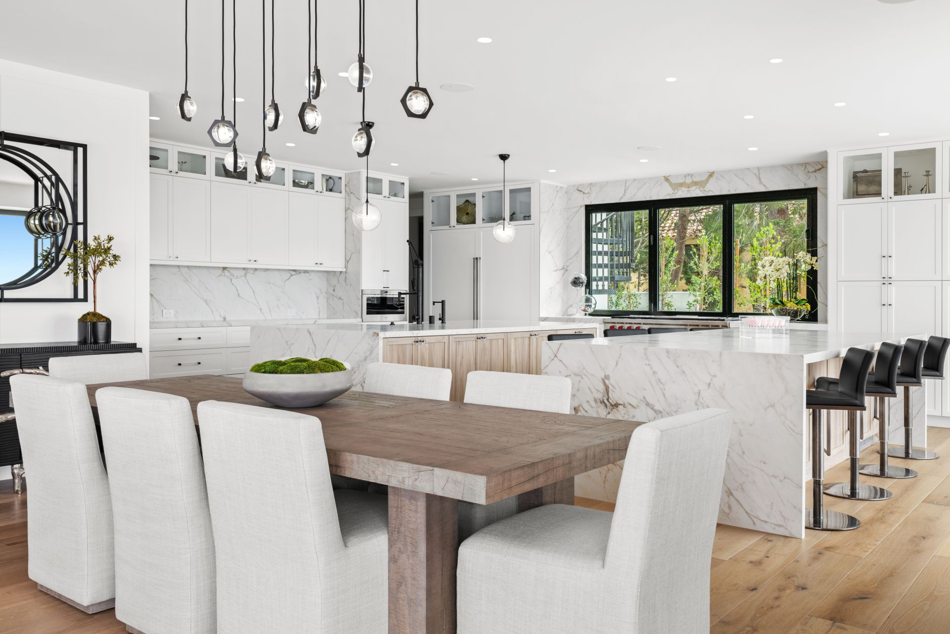 Modern kitchen with white cabinets, a wooden dining table, a marble island with bar stools, and pendant lighting.
