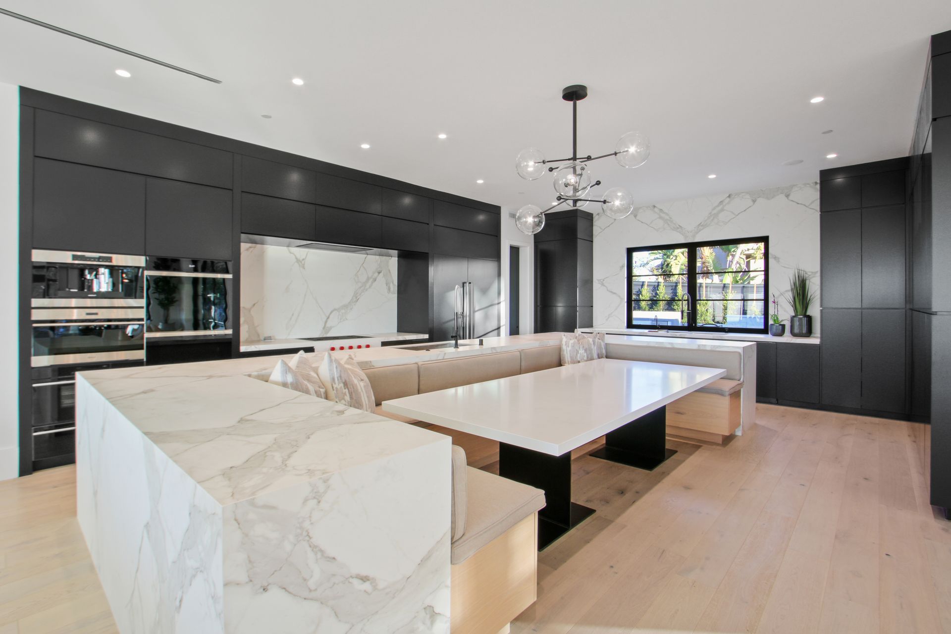 A modern kitchen features black cabinetry, a white marble kitchen island with integrated bench seating, and light wood floors.