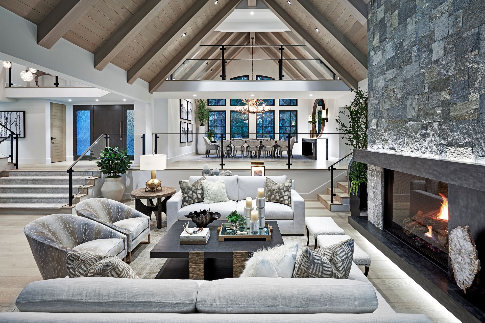 A bright, modern living room with a beige sofa, two armchairs, wooden coffee tables, and large windows overlooking the sea.