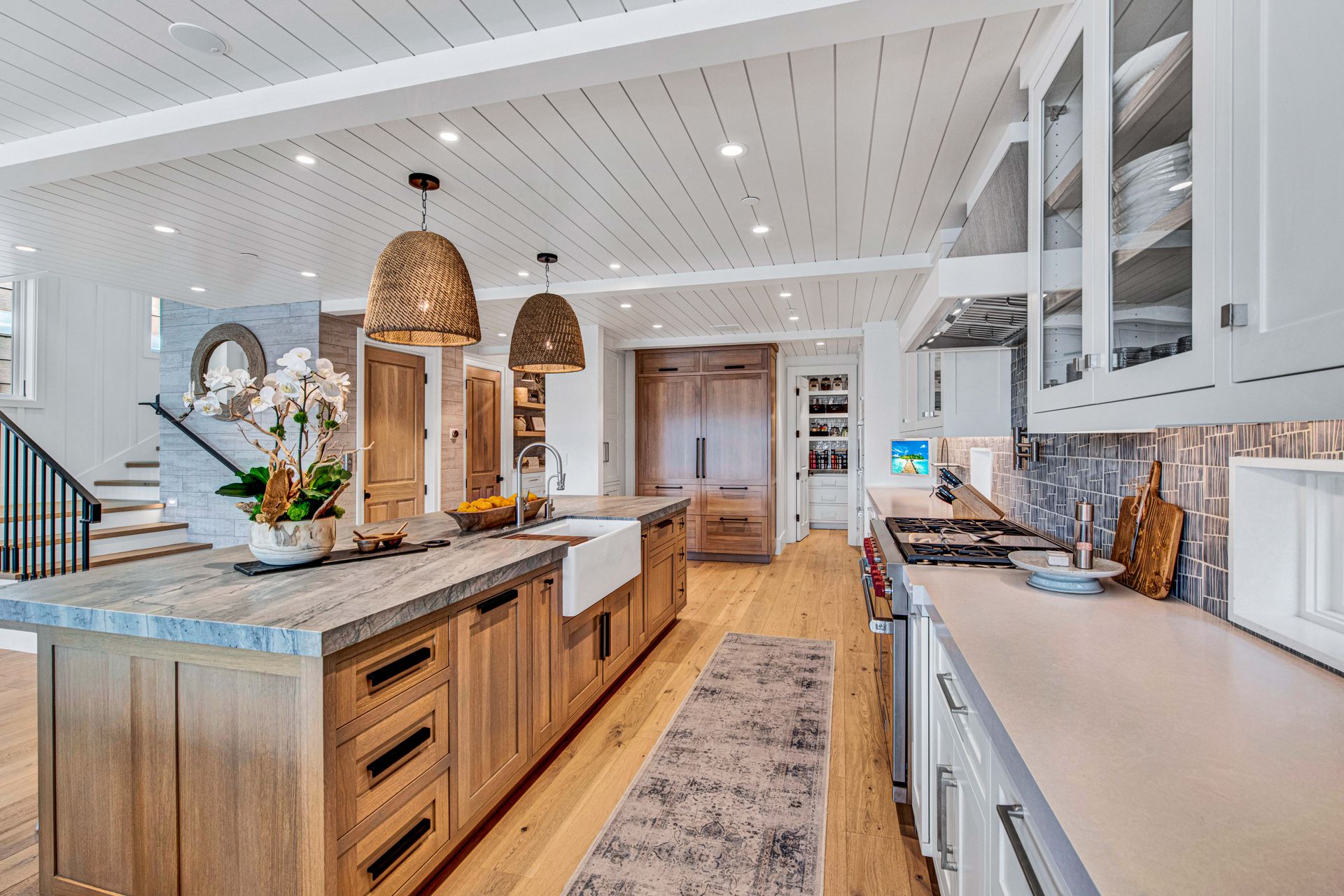 A spacious, bright kitchen featuring a large wooden island, white cabinetry, light wood floors, and two woven pendants.