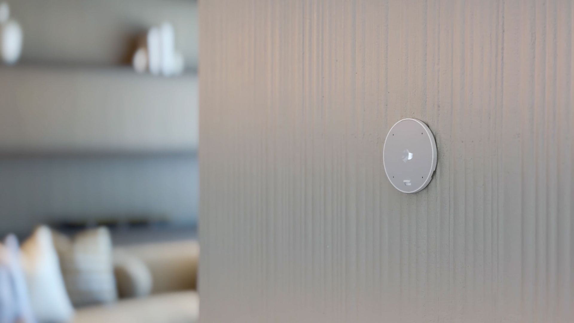 A smart home control panel displaying device settings sits on a wooden surface next to a decorative jar.