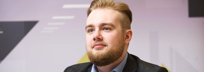 A man with light hair and a beard, in a suit, looks forward in a business setting.