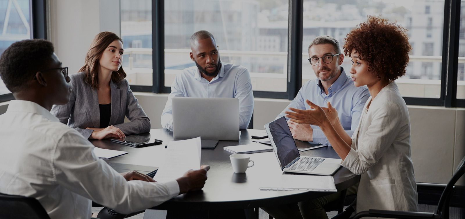 People in a meeting at a conference table with laptops and documents; discussing a presentation.