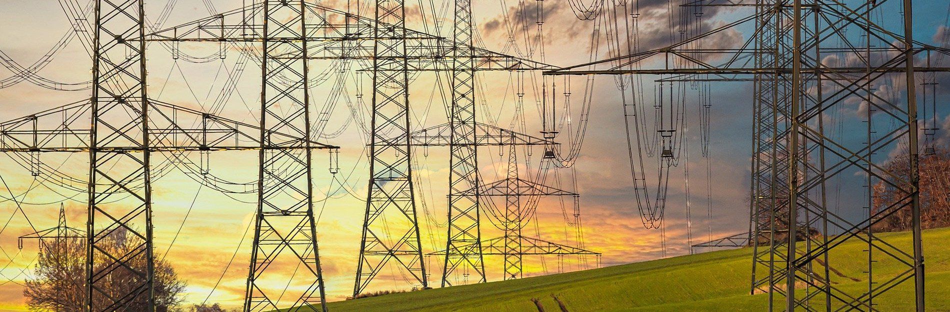 Power lines stretch across a green field with a colorful sunset sky in the background.