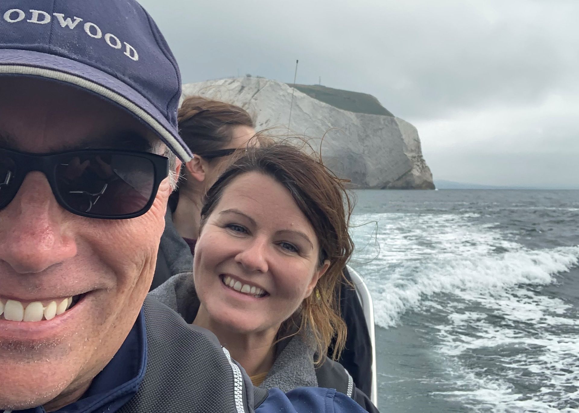 People smiling on a boat, with a rocky island in the background. Cloudy sky and choppy water.