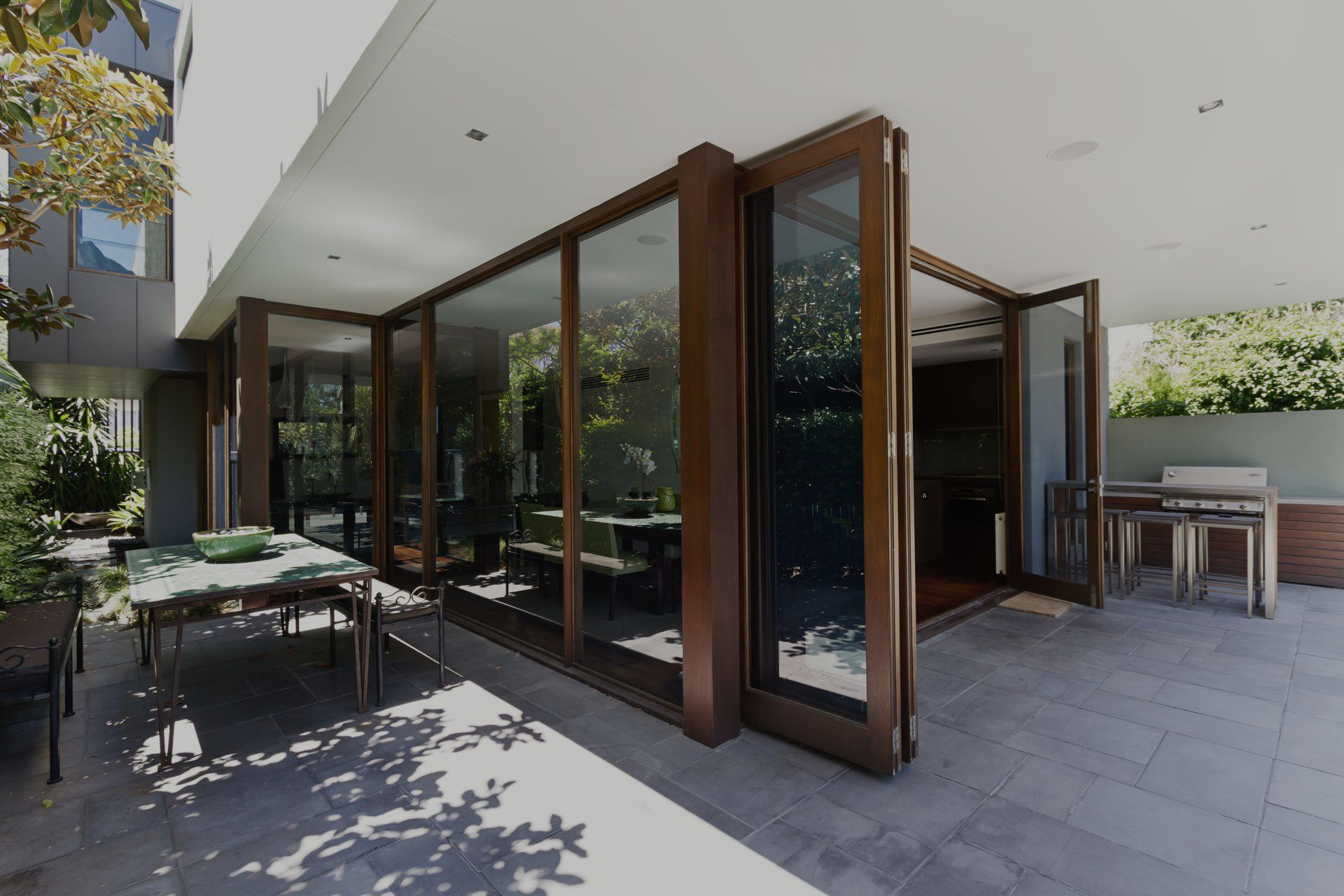 Patio with open folding glass doors, outdoor dining table, and stone flooring.