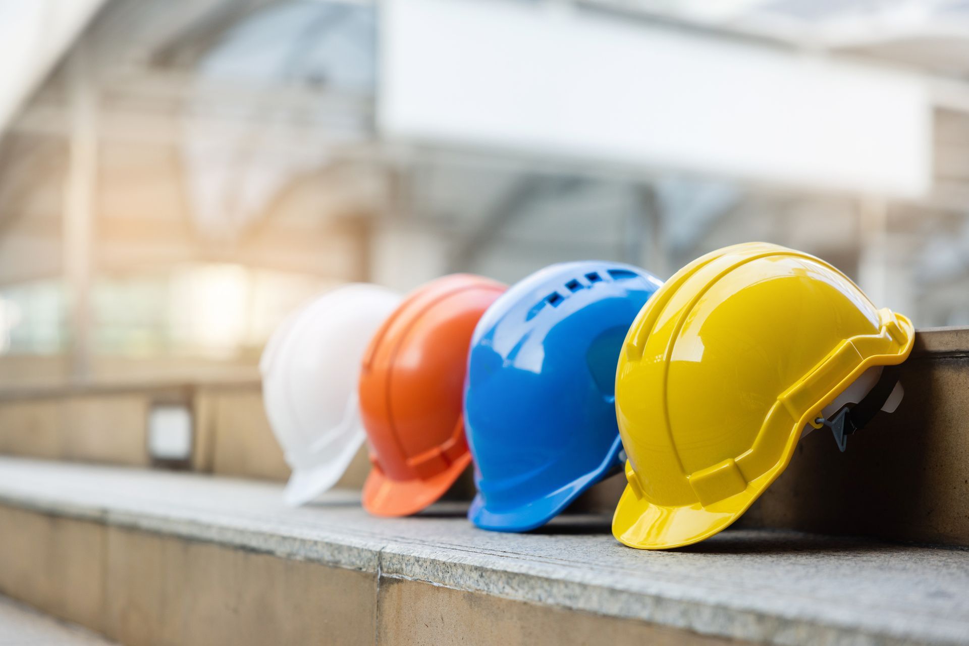 Four colorful construction hard hats lined up on a concrete step.