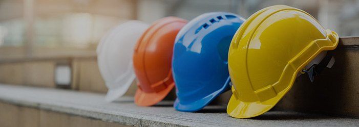 Four colorful construction hard hats in a row: white, orange, blue, and yellow.