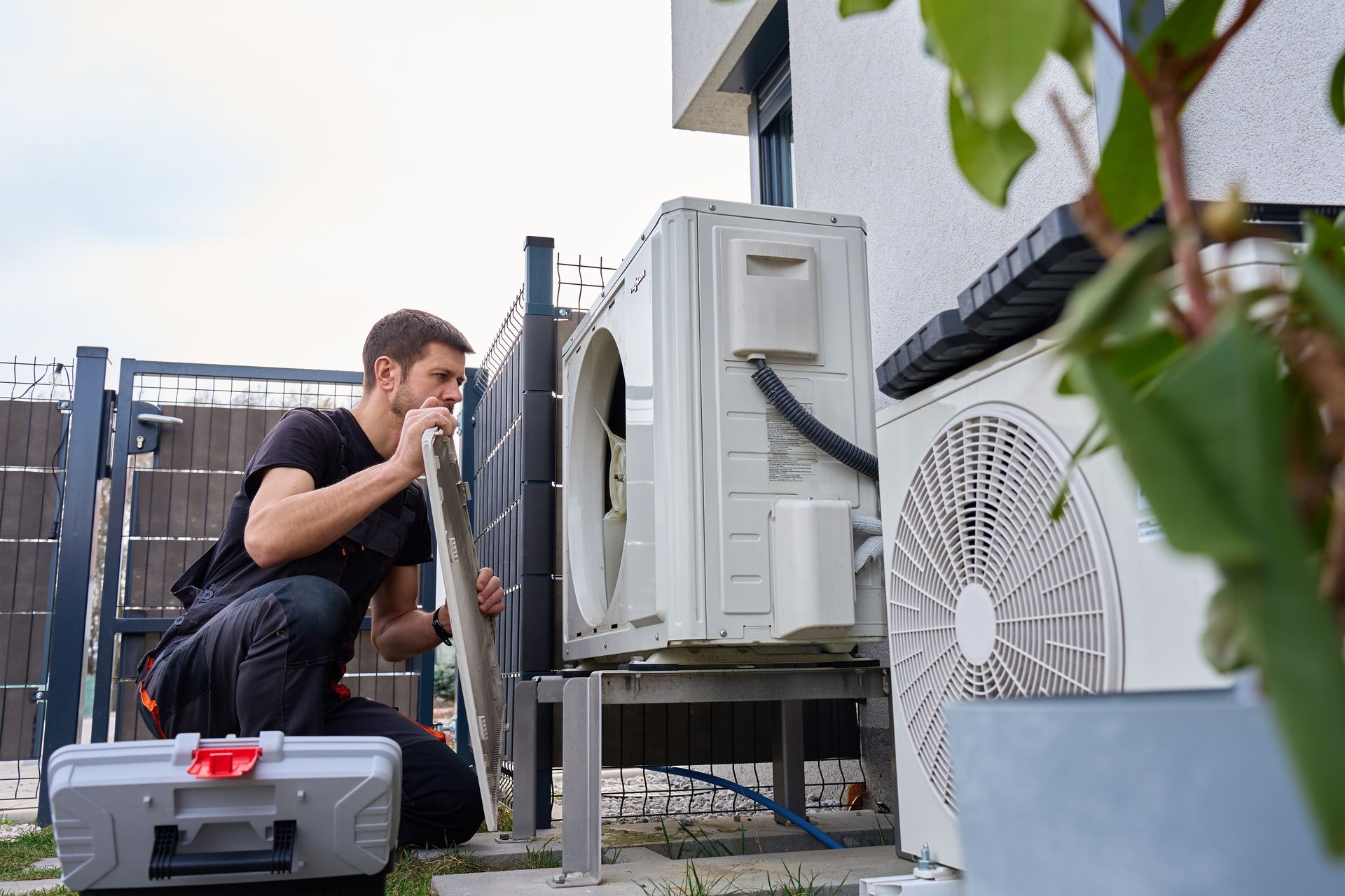 A technician inspecting an outdoor air conditioning unit beside a building.
