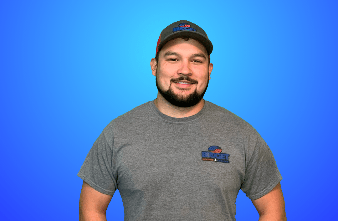 A person wearing a grey t-shirt and baseball cap smiles against a solid blue background.
