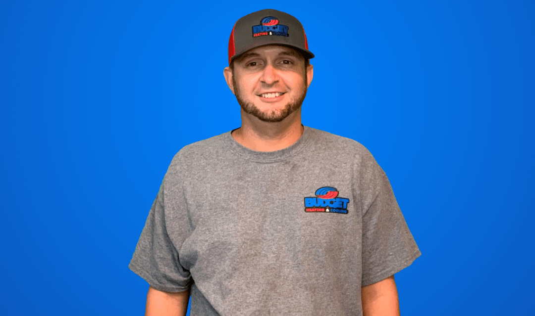 A person wearing a grey t-shirt and baseball cap with a company logo against a solid blue background.