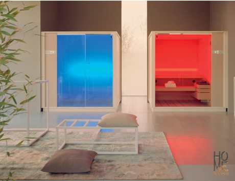 Stanza moderna con due cabine illuminate, una blu e una rossa, accanto a un tavolino basso bianco e cuscini su un tappeto.