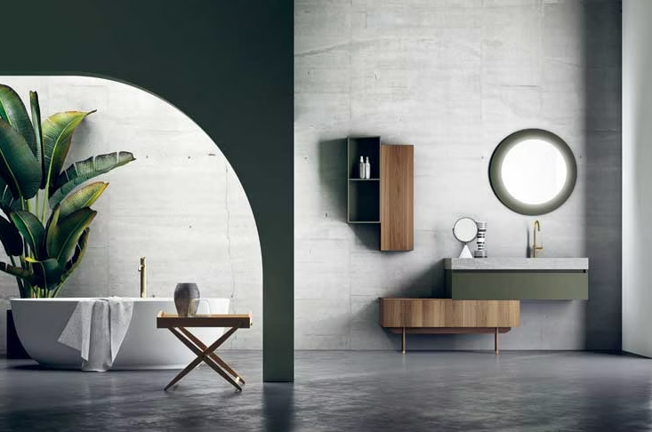 Bagno minimalista con specchio rotondo, mobiletto in legno e pianta in vaso su pareti grigie.