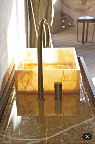 Lavabo da bagno moderno con rubinetto dorato e vasca rettangolare color ambra su piano in marmo.