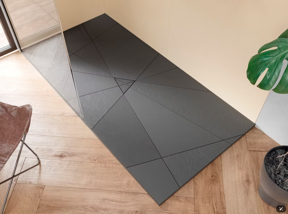 Tappetini in schiuma nera disposti in un angolo su un pavimento in legno chiaro, accanto a una parete beige e una sedia.